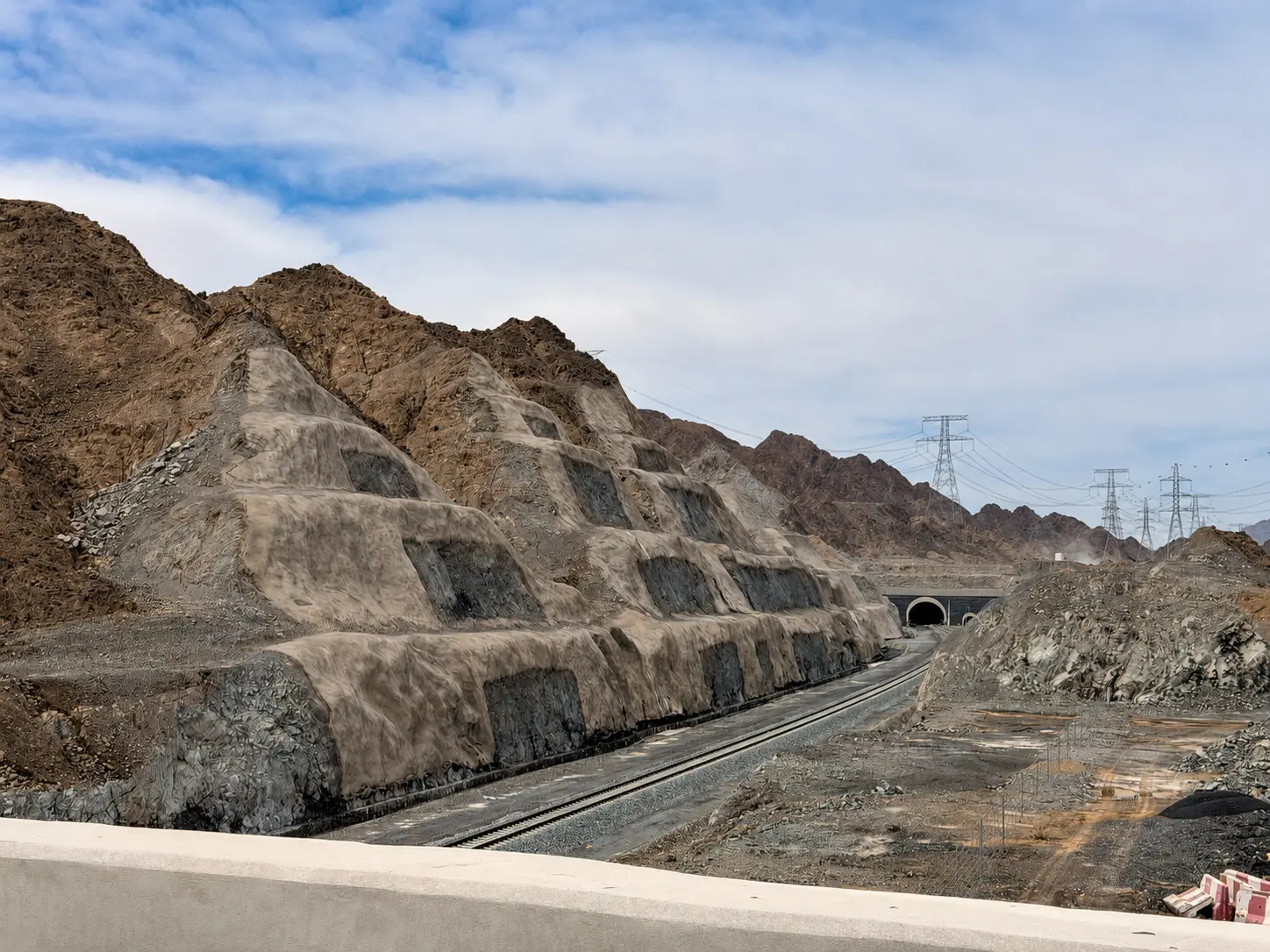 Etihad Rail railway tracks leading towards a mountain tunnel portal beneath stepped benched rock slopes